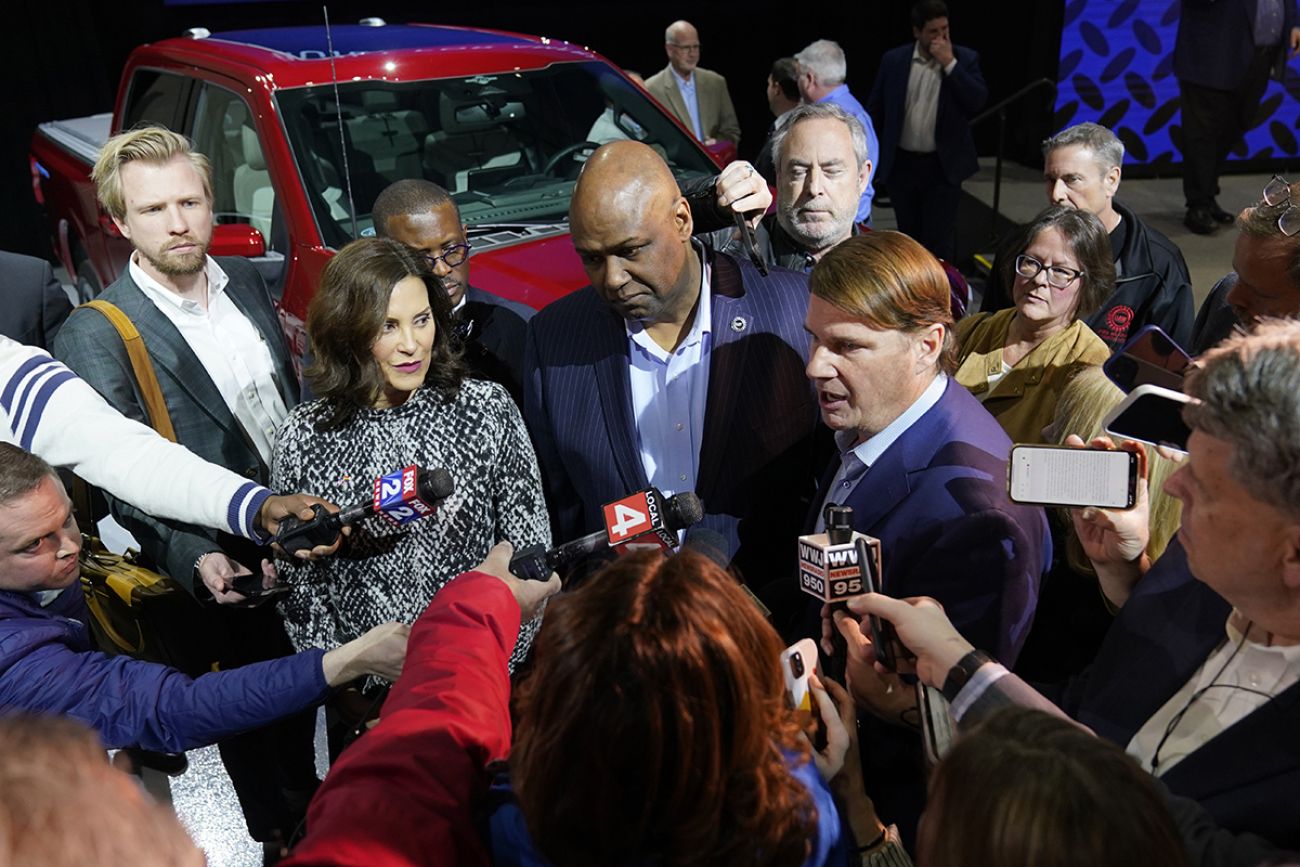 Michigan Gov. Gretchen Whitmer at a press conference. Reporters surround her and others.