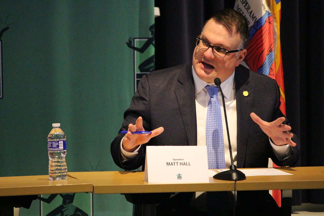Matt Hall speaking into a microphone at a press conference. 