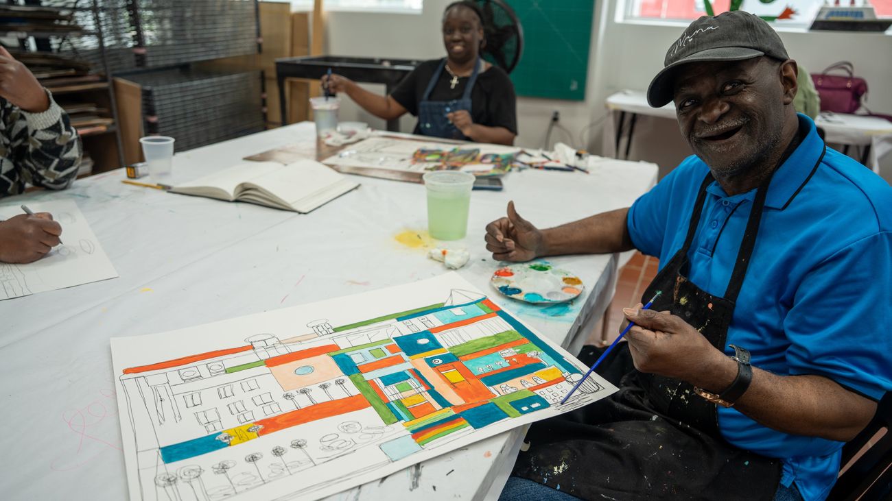 Ray Smith sits at a table while he paints. 