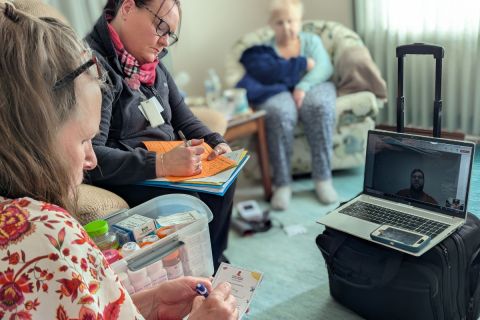 Two women take notes while taking to a pharmacist on a laptop. 