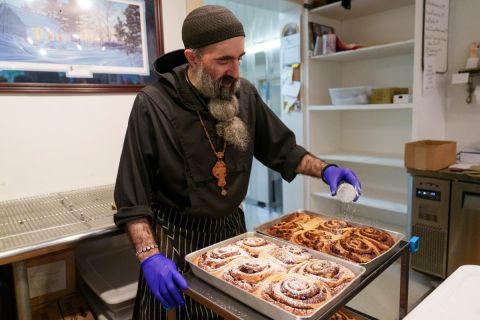 A man sprinkles powdered sugar over panfuls of pastries