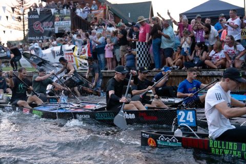 Canoe racers paddle down the Au Sable River while a crowd of spectators looks on