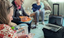 Two women take notes while taking to a pharmacist on a laptop. 