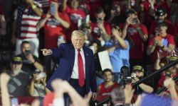 President Donald Trump walks on stage. People are behind him.